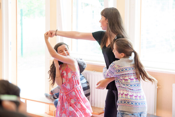Eine Freiwillige des FSJs tanzt und spielt mit zwei Kindern.